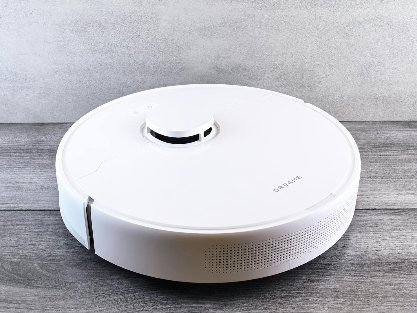 Vit Dreame robotdammsugare på ett grått trägolv.