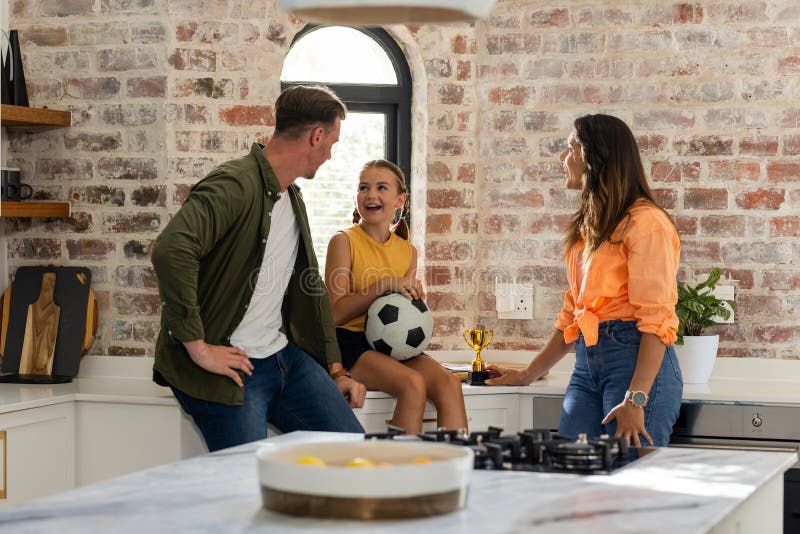 En fotbollsfamilj i köket firar en vinst med pokal och fotboll.