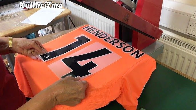 En värmepress används för att trycka namn och nummer på en orange fotbollströja.